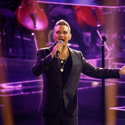 Robbie Williams steht in einem schwarzen Anzug auf der Bühne.