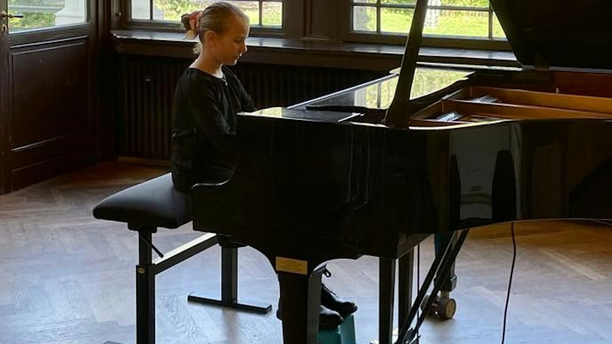Lilly Emilia Schönknecht beim Klavierspiel, die Füße auf einem Höckerchen.