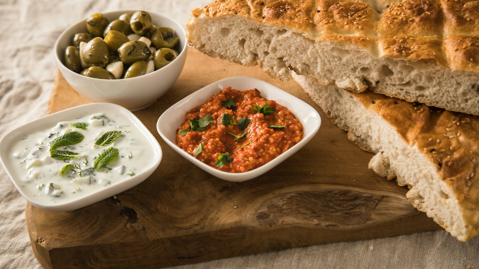 Zwei Brotaufstriche in kleinen Schälchen angerichtet, daneben liegt Fladenbrot, im Hintergrund steht ein Schälchen mit Oliven
