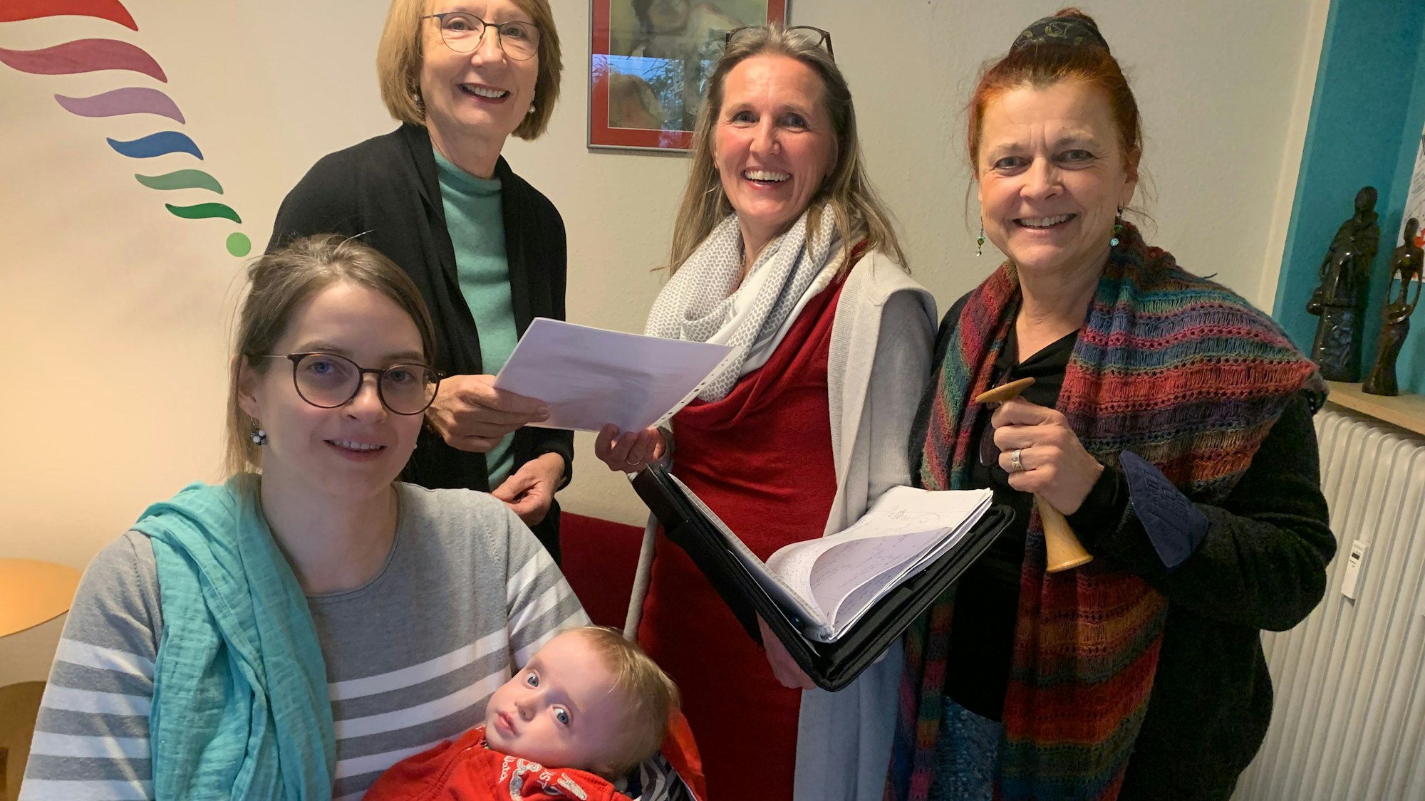 Judith Wittköpper sitzt am Tisch, ihr Baby im Arm, die anderen Frauen stehen hinter ihr. Sie lächeln in die Kamera.