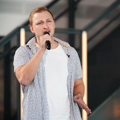 David steht auf einer Bühne und singt in ein Mikro.