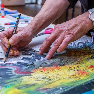 Zwei ältere Hände malen ein Bild, das mit Zeitungspapier unterlegt ist