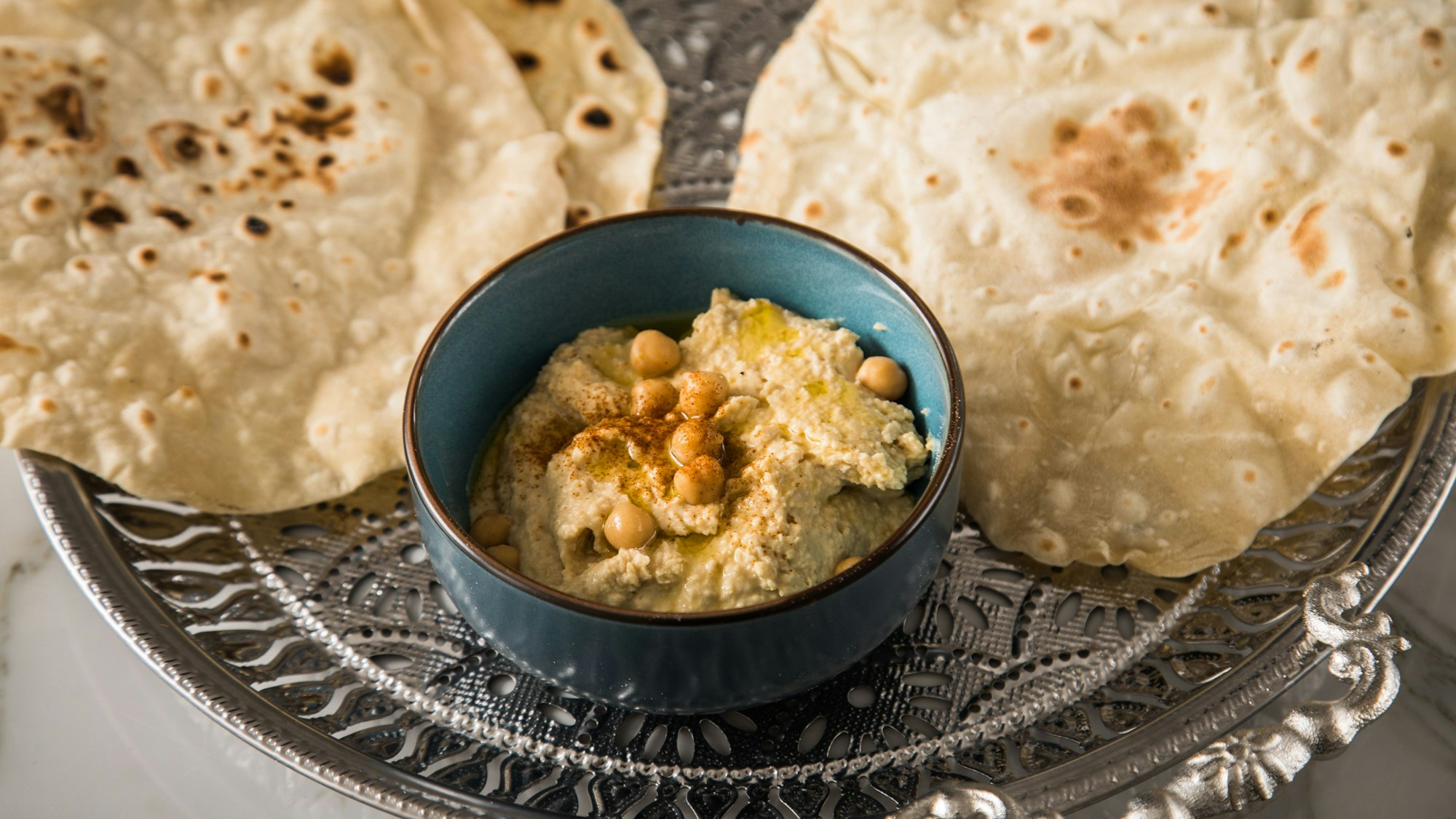 Hummus in einem Schälchen, daneben zwei Fladenbrote