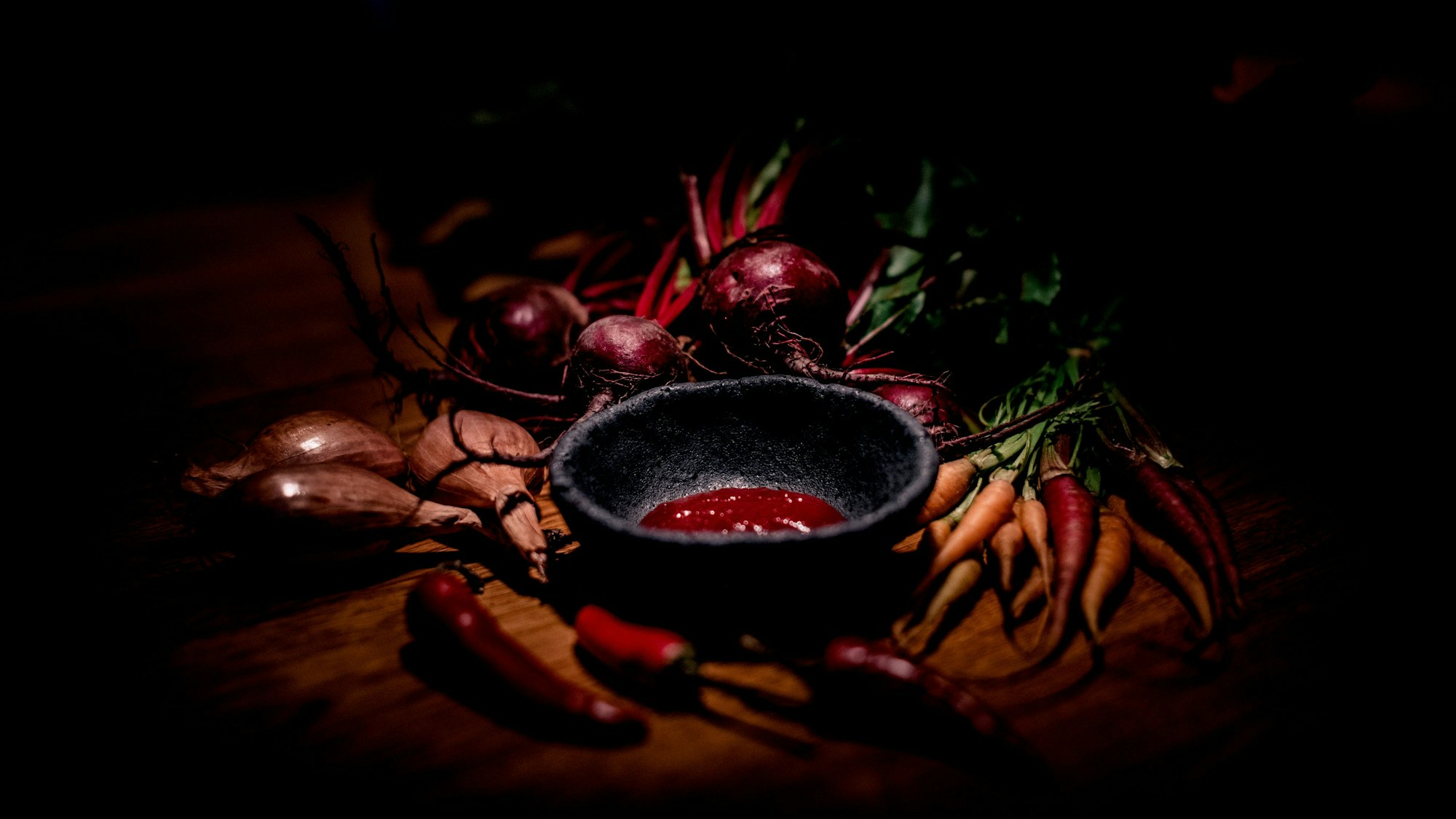 Ein roter Aufstrich ist in einem Schälchen angerichtet, umrundet von verschiedenen Gemüsesorten wie Karotten, Zwiebeln und Chillischoten.