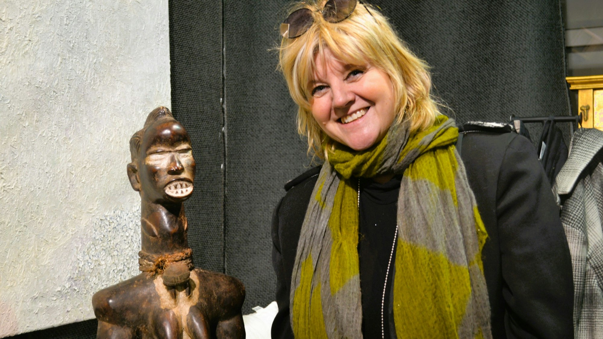Eine Botique Besitzerin steht grinsend neben einem afrikanischen Ausstellungsstück.