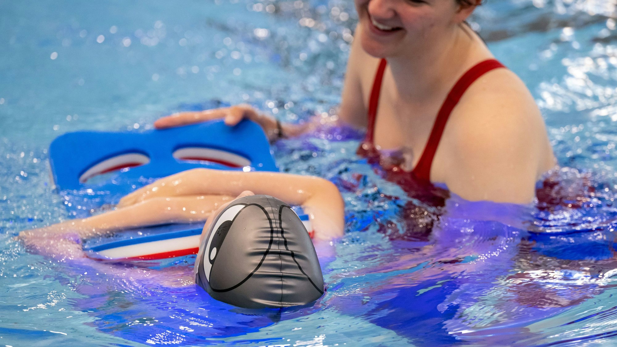 Ein Junge hält sich in einem Schwimmbad mit einem Schwimmbrett über Wasser.
