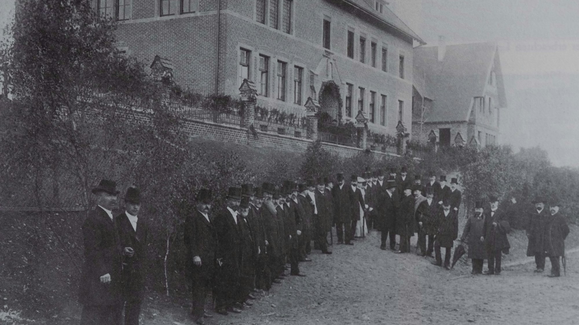 Zu sehen ist ein historisches Foto mit Männern in Frack und Zylinder.