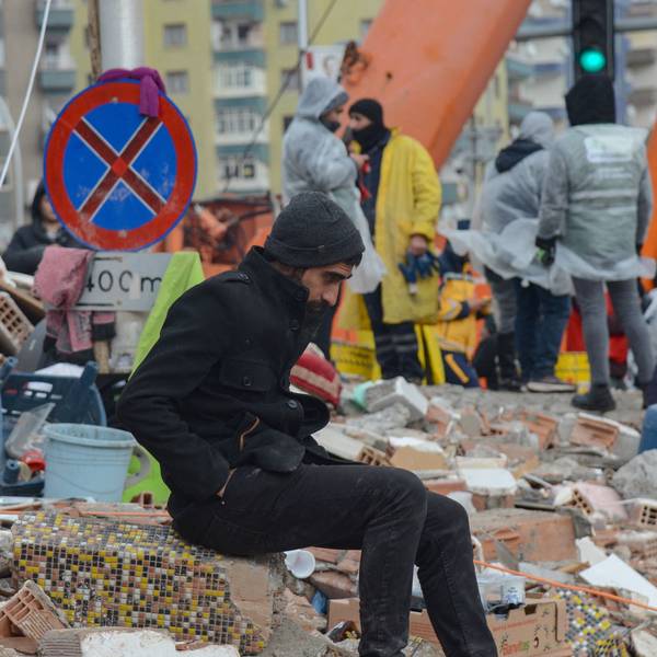 Ein Mann verschnauft im türkischen Diyarbakir während im Hintergrund Rettungskräfte in Schuttbergen arbeiten.