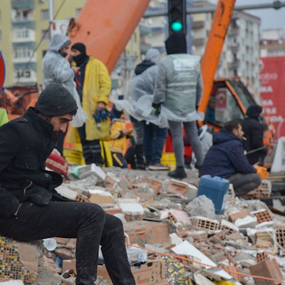 Ein Mann verschnauft im türkischen Diyarbakir während im Hintergrund Rettungskräfte in Schuttbergen arbeiten.