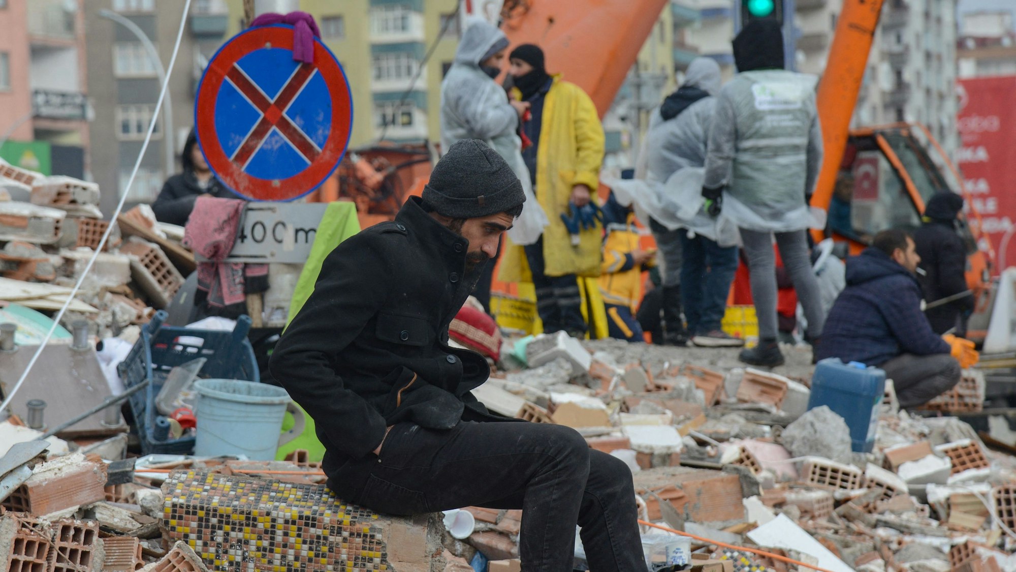 Ein Mann verschnauft im türkischen Diyarbakir während im Hintergrund Rettungskräfte in Schuttbergen arbeiten.