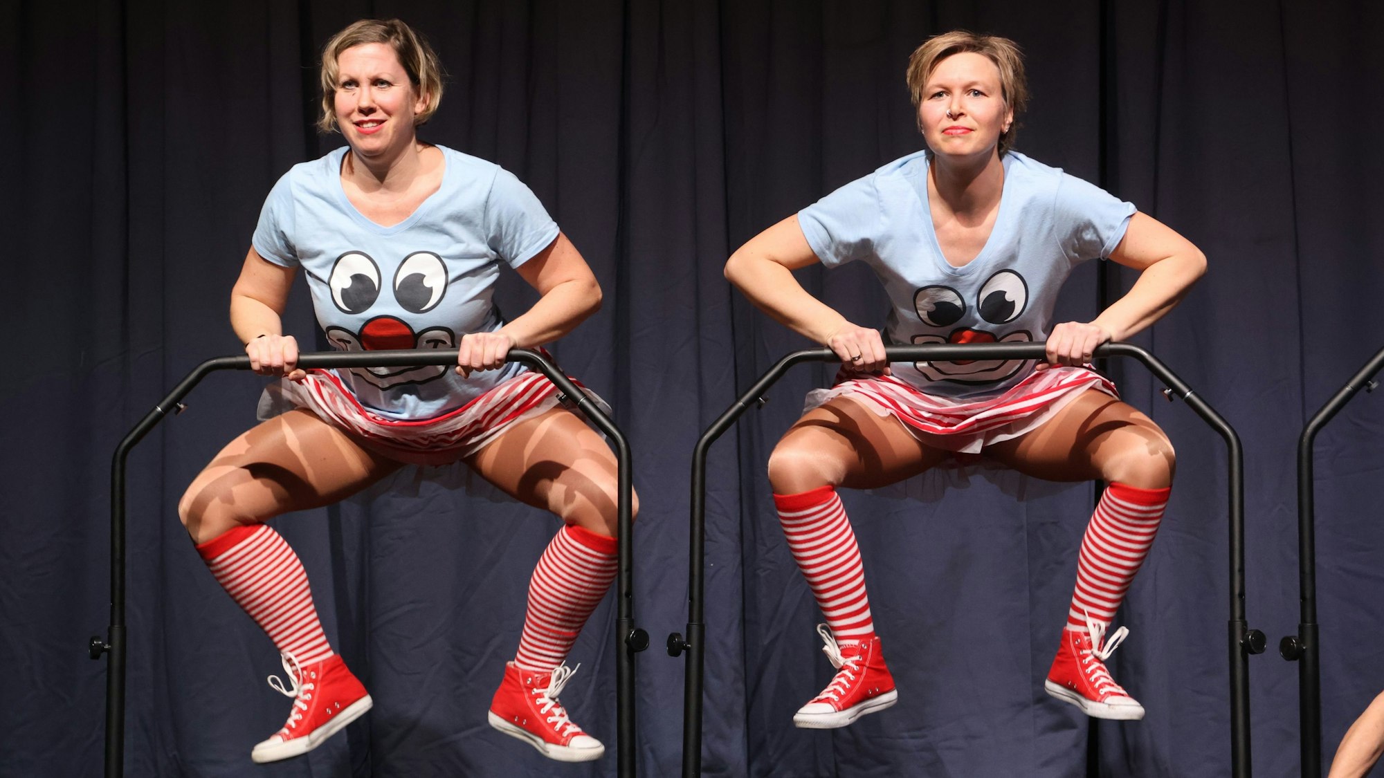 Zwei karnevalistisch verkleidete Frauen springen Trampolin und halten sich dabei an Stangen fest.