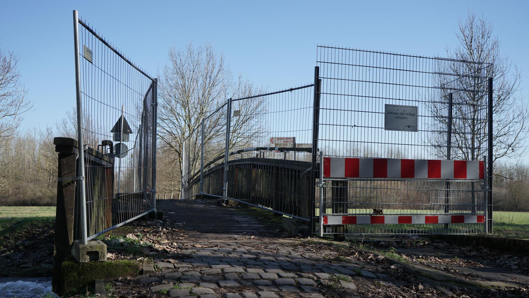 Man sieht eine schmale Brücke über ein Gewässer, welche an den Geländern durch Bauzäune begrenzt wird.