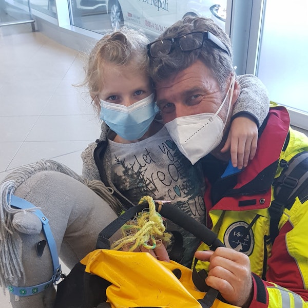 man sihet Vater und Tochter, wie sie in die Kamera gucken, sie tragen Masken. Ingo hat sich neben Mia gekniet, diese hat den Arm um seinen Hals.