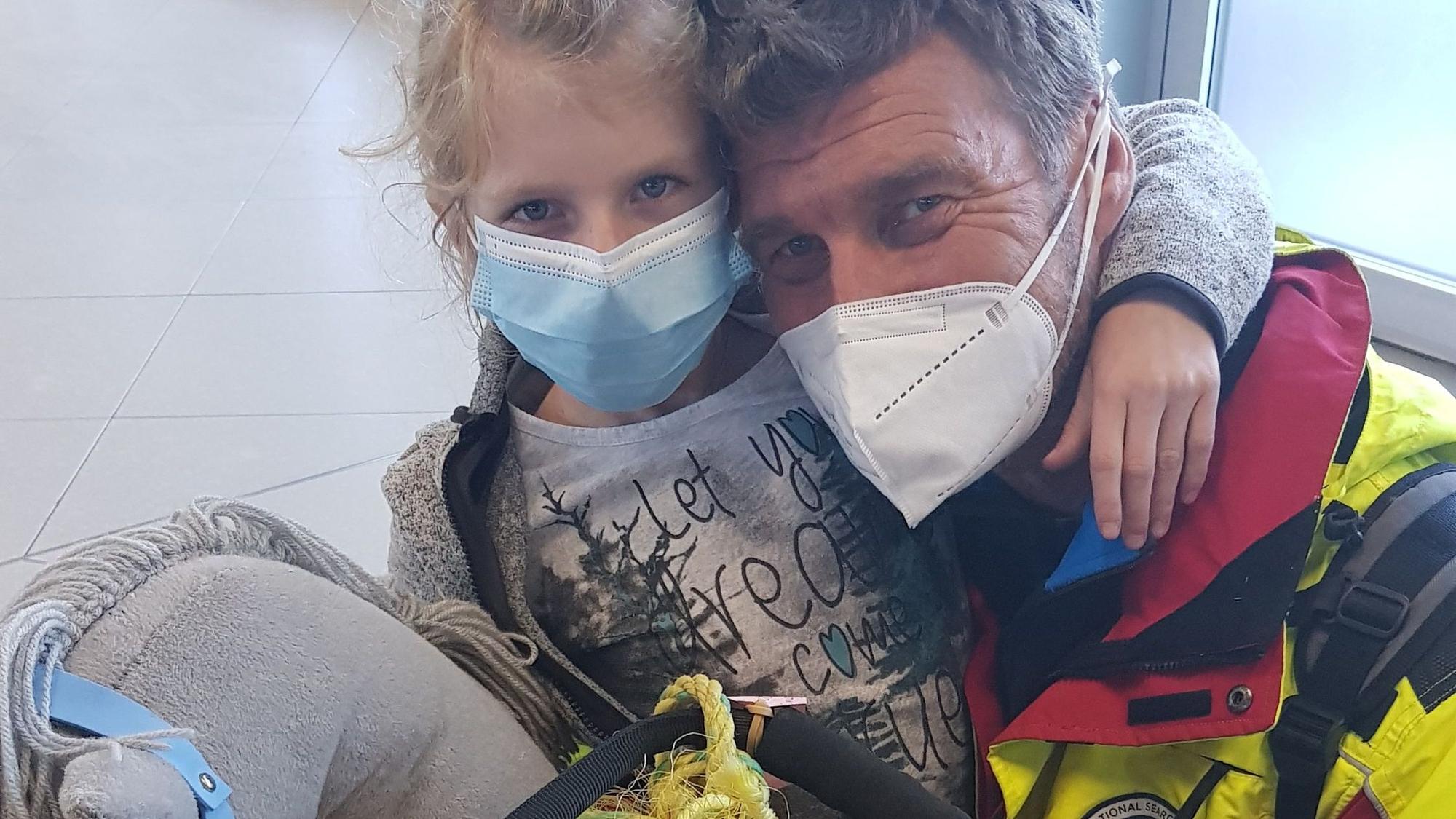 man sihet Vater und Tochter, wie sie in die Kamera gucken, sie tragen Masken. Ingo hat sich neben Mia gekniet, diese hat den Arm um seinen Hals.