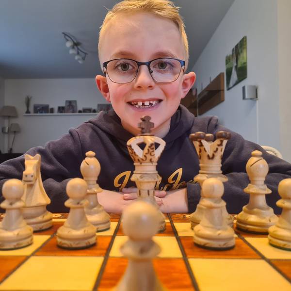 Nick sitzt hinter einem Schachbrett mit Figuren und schaut in die Kamera.