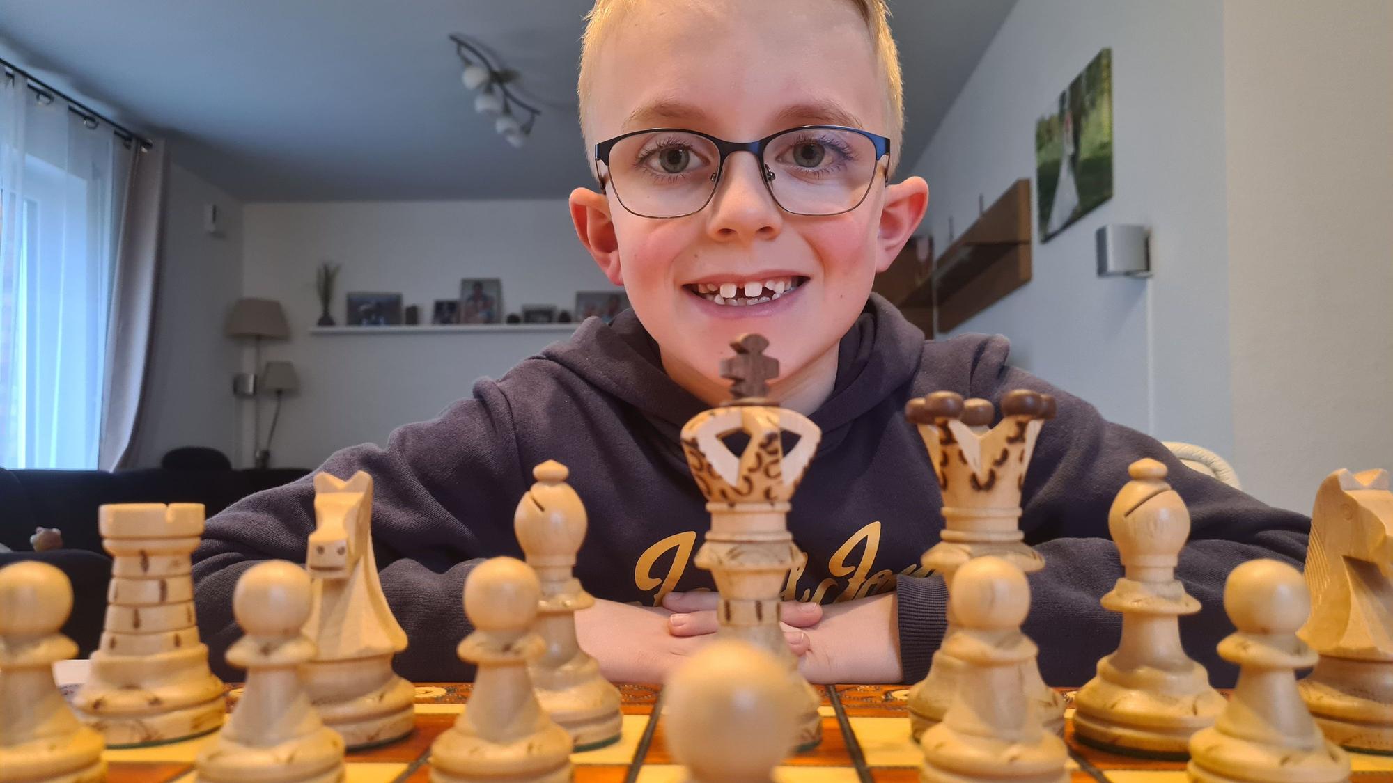 Nick sitzt hinter einem Schachbrett mit Figuren und schaut in die Kamera.