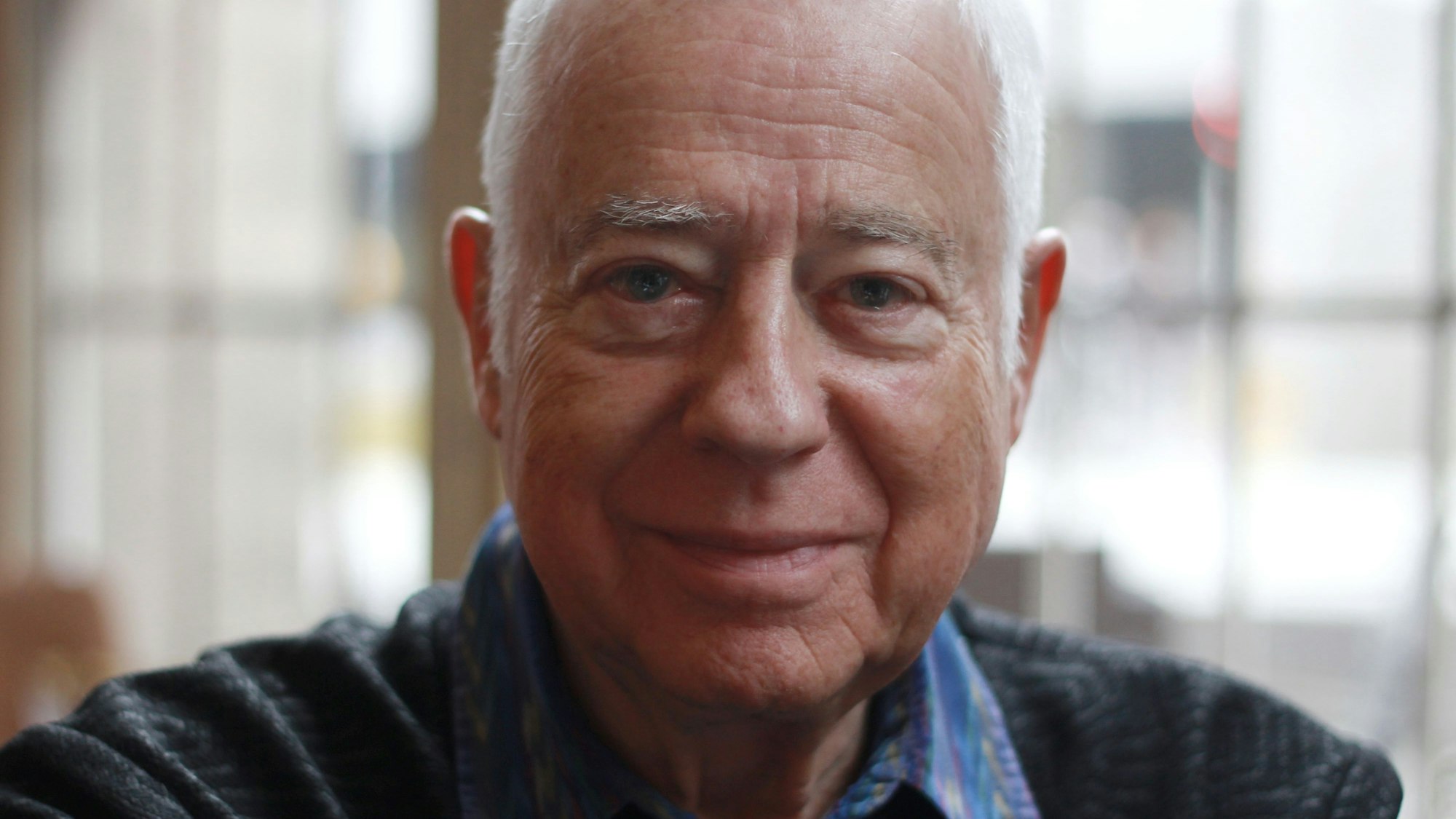 Nahaufnahme des betagten Opernintendanten, er schaut in die Kamera.