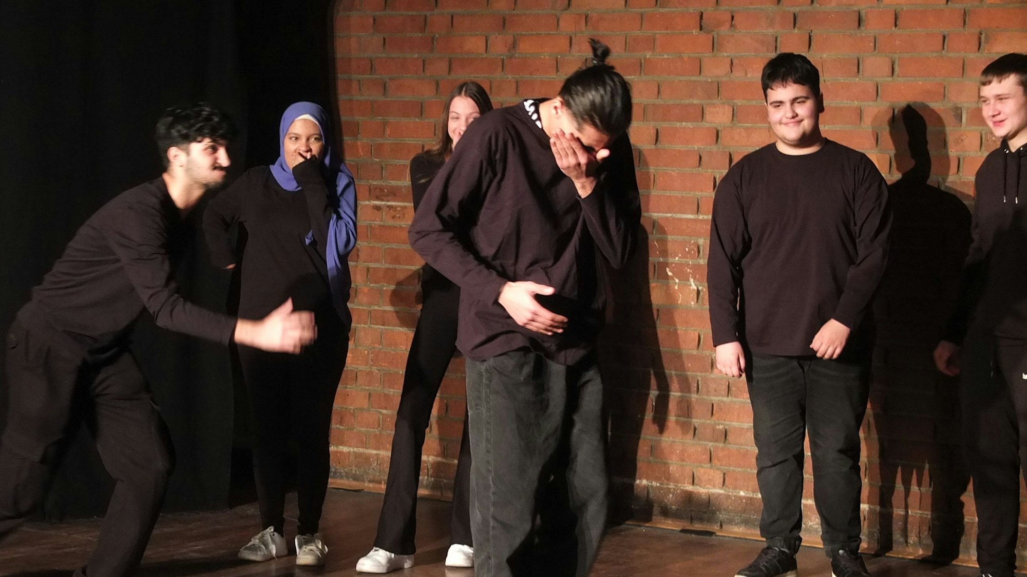 Ein Schüler steht in der Mitte der Bühne und hält die Hände vors Gesicht, er wird ausgelacht und gehändelt.