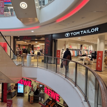 Eine Frau geht am Geschäft von Tom Tailor vorbei. Daneben befindet sich das Geschäft von S.Oliver.