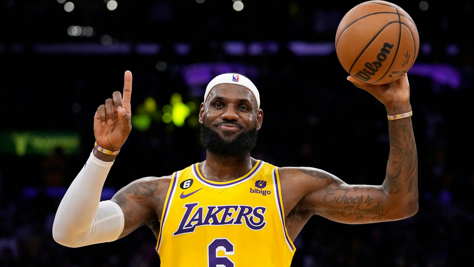 LeBron James lächelt zufrieden, zeigt mit dem Zeigefinger eine Eins und hält in der anderen Hand einen Basketball.