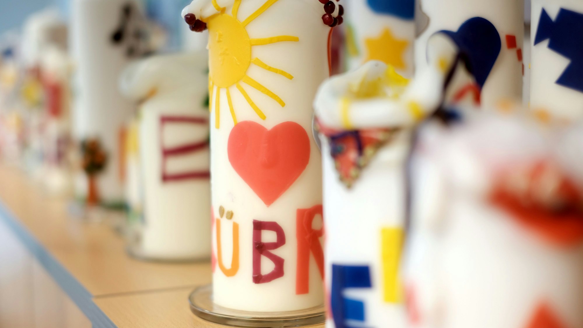 Bunte Kerzen stehen in einer langen Reihe auf einem Regal.