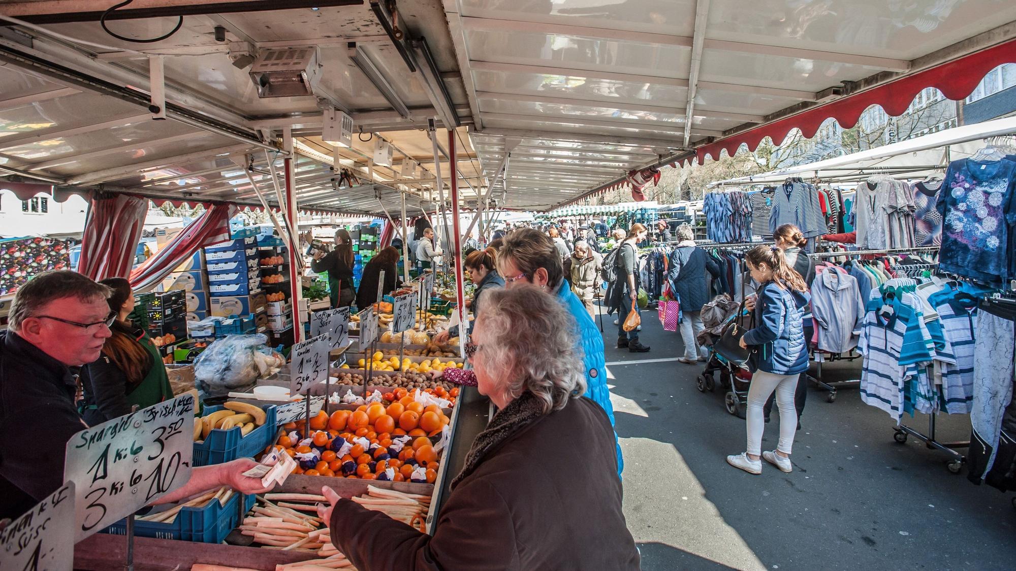Kundinnen kaufen an einem Marktstand Spargel.