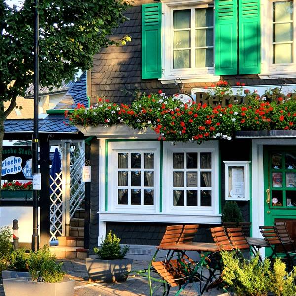 Foto eines Gasthauses in Burscheid mit Blumen und Biergartenstühlen.