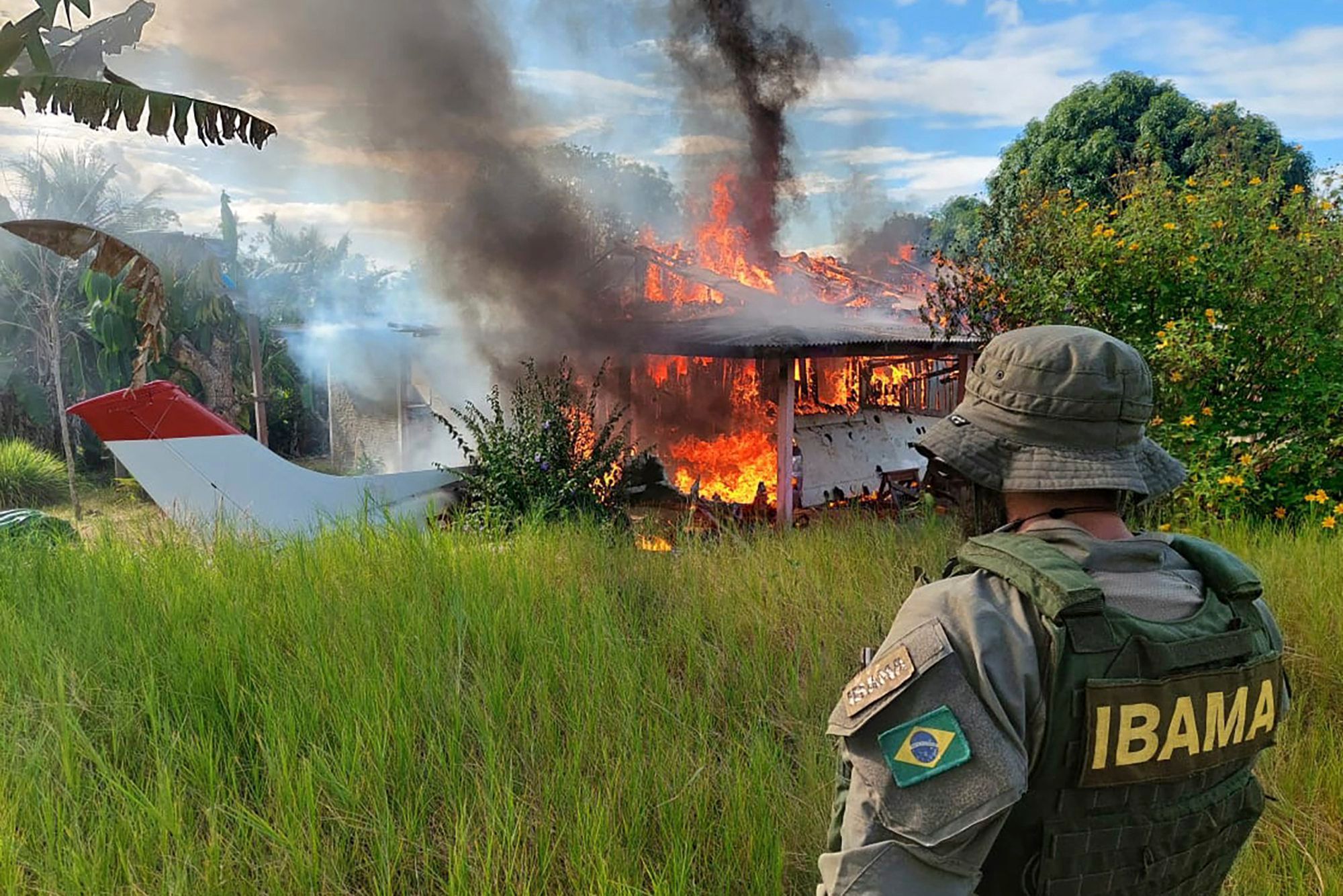 Auf diesem von der brasilianischen Umweltbehörde IBAMA zur Verfügung gestellten Bild sieht ein Beamter zu, wie ein Gebäude und ein Flugzeug, die Bergleuten gehören, im Gebiet der Yanomami-Indigenen im brasilianischen Bundesstaat Roraima in Flammen aufgehen.