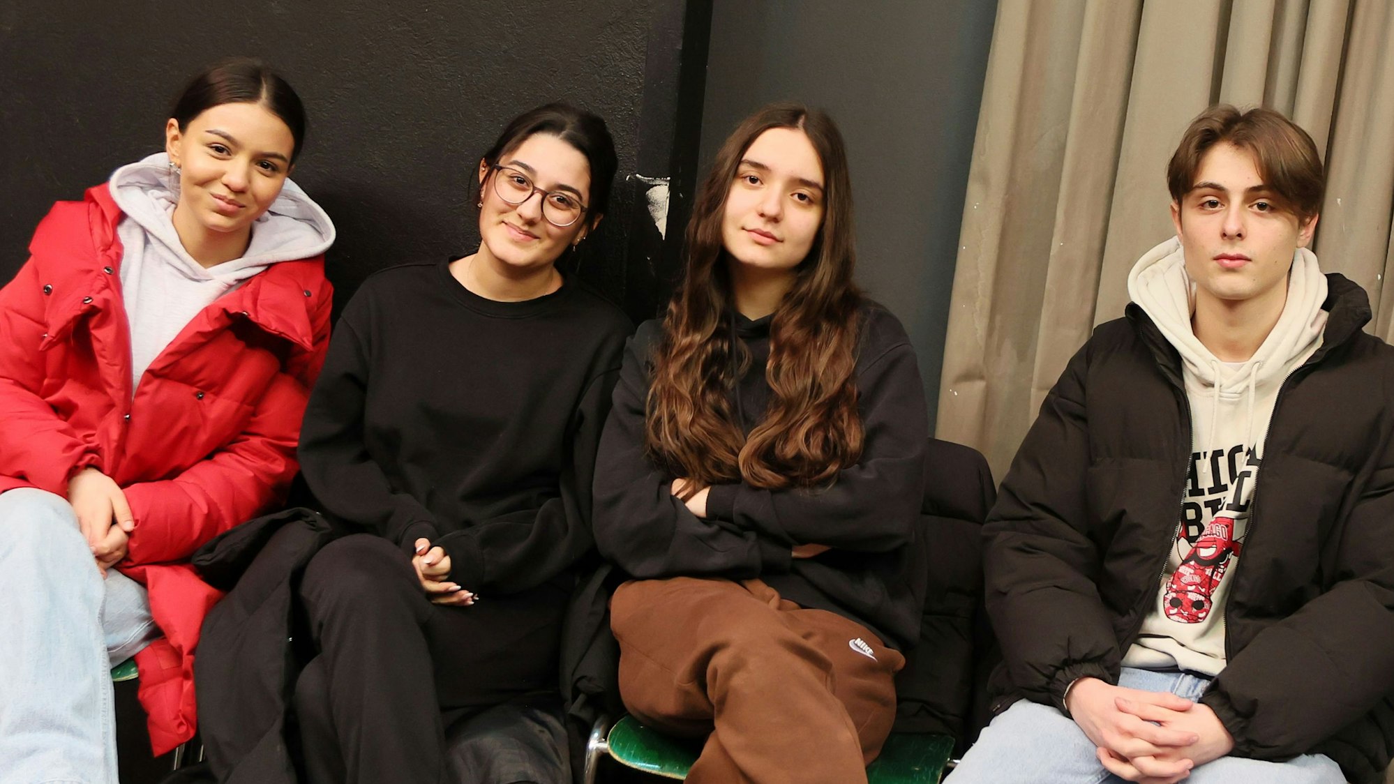 Eine Gruppe von Schülern (drei Schülerinnen und ein Schüler) sitzen auf Stühlen.