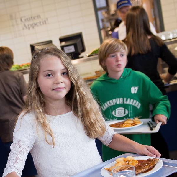 Schüler tragen in der Mensa der Gesamtschule Barmen in Wuppertal (Nordrhein-Westfalen) Tabletts mit Essen zu ihren Plätzen.