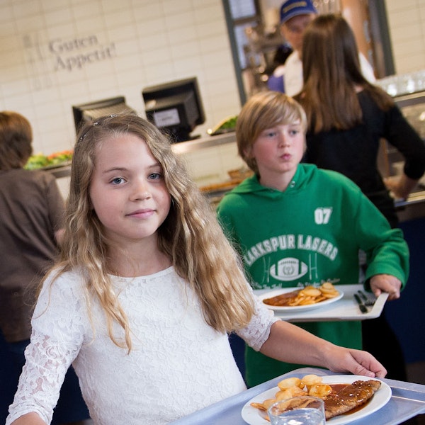 Schüler tragen in der Mensa der Gesamtschule Barmen in Wuppertal (Nordrhein-Westfalen) Tabletts mit Essen zu ihren Plätzen.
