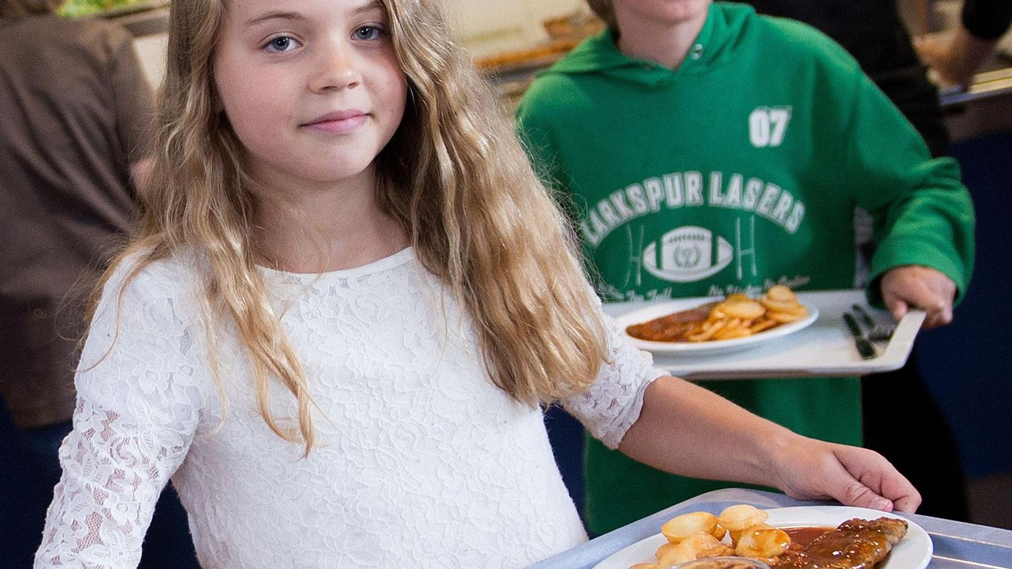 Schüler tragen in der Mensa der Gesamtschule Barmen in Wuppertal (Nordrhein-Westfalen) Tabletts mit Essen zu ihren Plätzen.