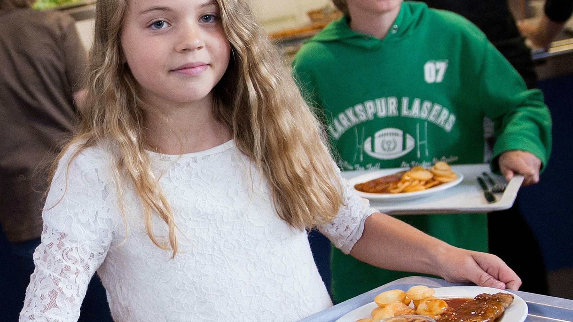Schüler tragen in der Mensa der Gesamtschule Barmen in Wuppertal (Nordrhein-Westfalen) Tabletts mit Essen zu ihren Plätzen.