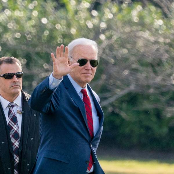 Präsident Joe Biden trägt eine Sonnenbrille und winkt in die Kamera.