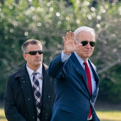 Präsident Joe Biden trägt eine Sonnenbrille und winkt in die Kamera.