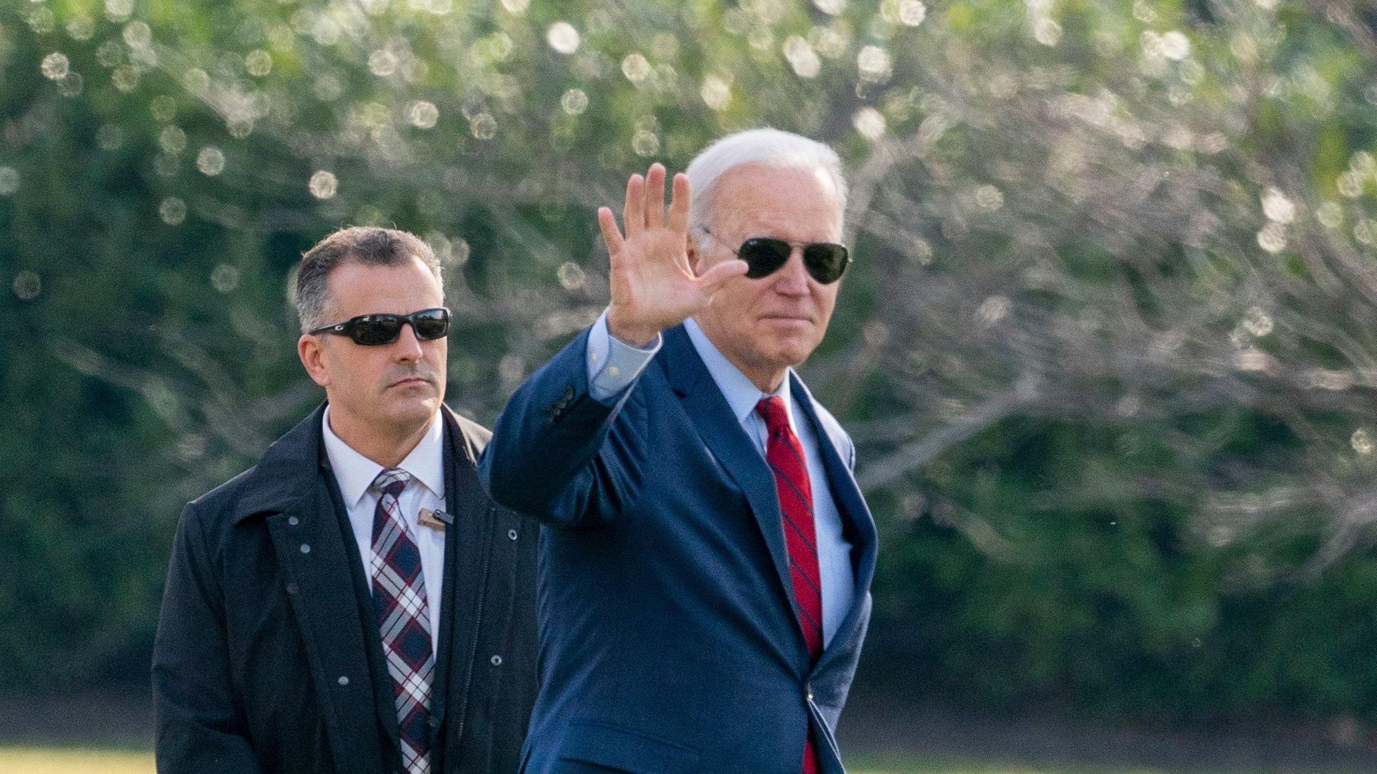 Präsident Joe Biden trägt eine Sonnenbrille und winkt in die Kamera.