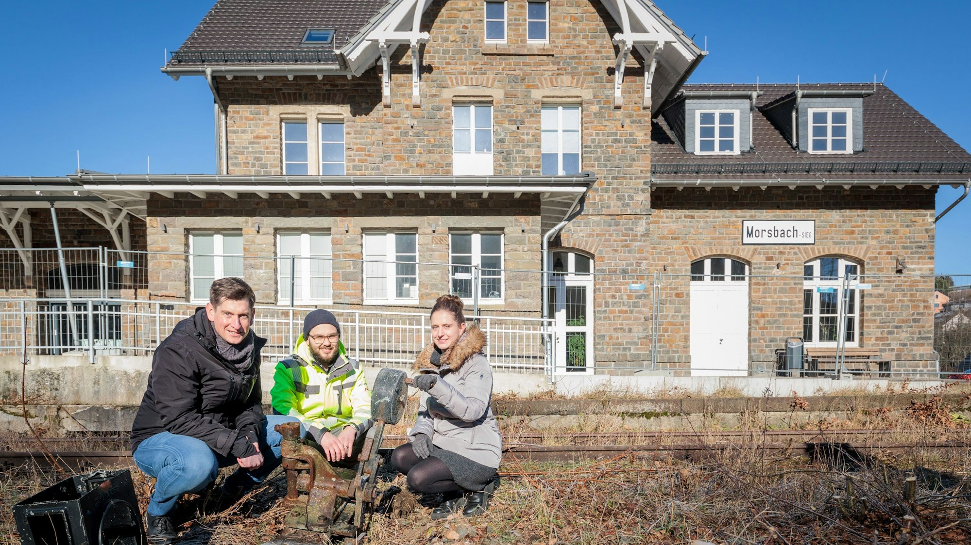 Drei Menschen knien vor dem alten Bahnhof in Morsbach.