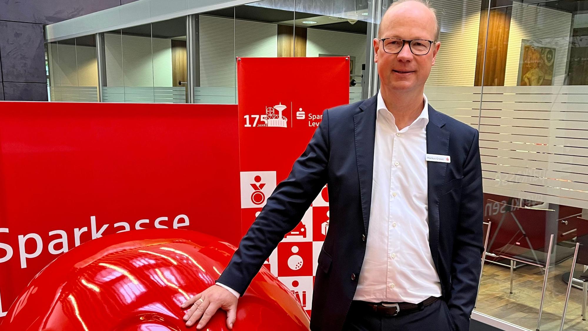 Markus Grawe, Vorstandschef der Sparkasse Leverkusen, steht an einem roten Sparschwein.