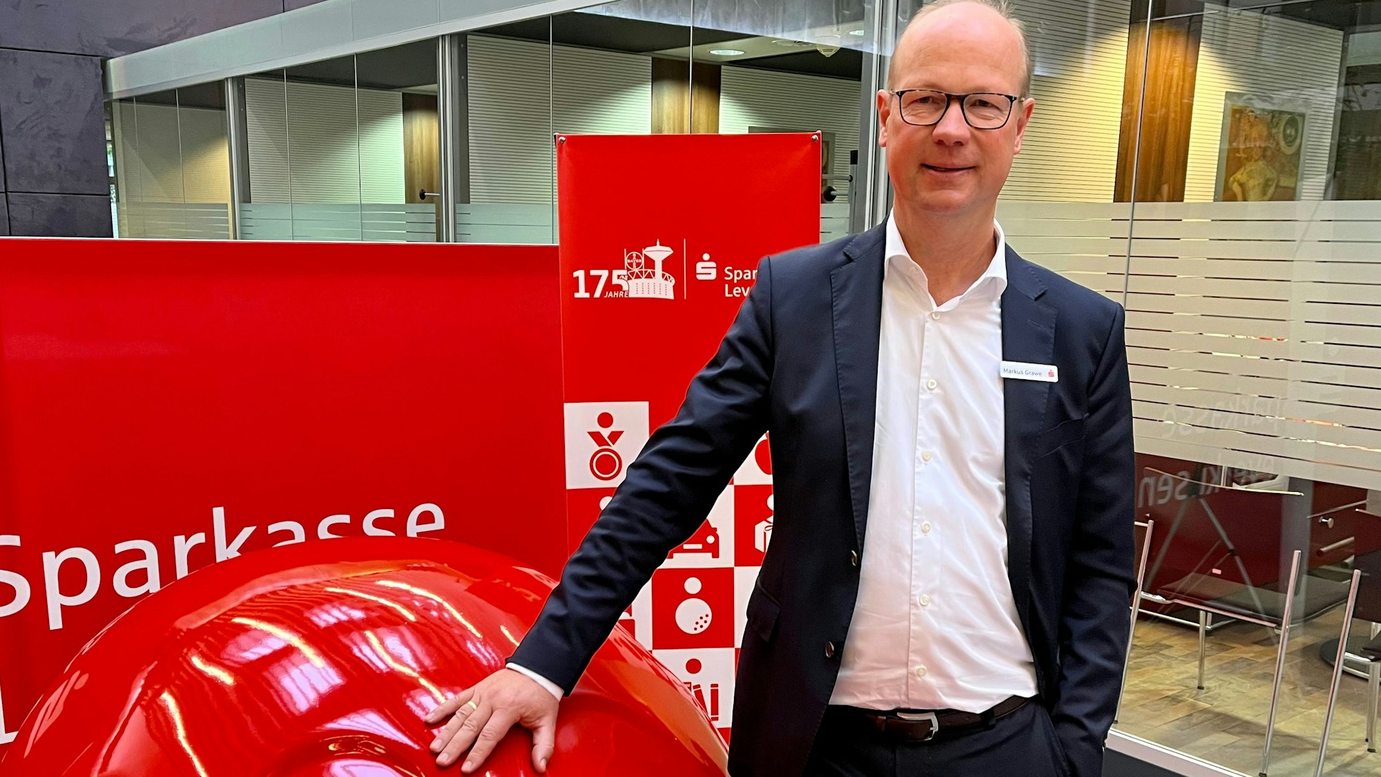 Markus Grawe, Vorstandschef der Sparkasse Leverkusen, steht an einem roten Sparschwein.