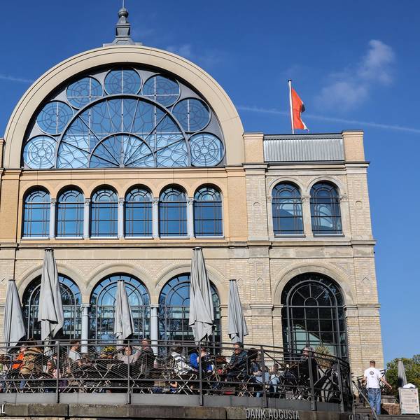 Auf der Terrasse vor dem Kölner Flora-Gebäude im gleichnamigen Botanischen Garten sitzen Menschen an Tischen.