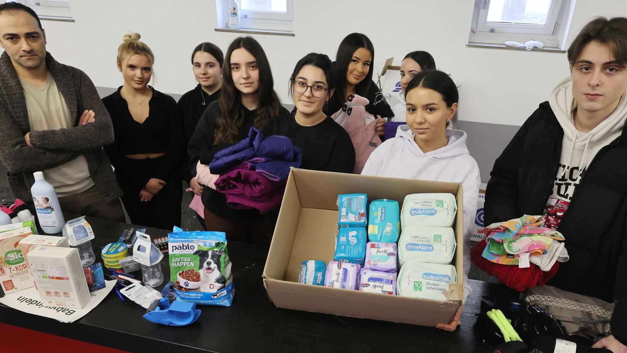 Ein Gruppe Schüler steht hinter einem langen Tisch, auf dem Hygieneartikel und andere Waren deponiert sind.