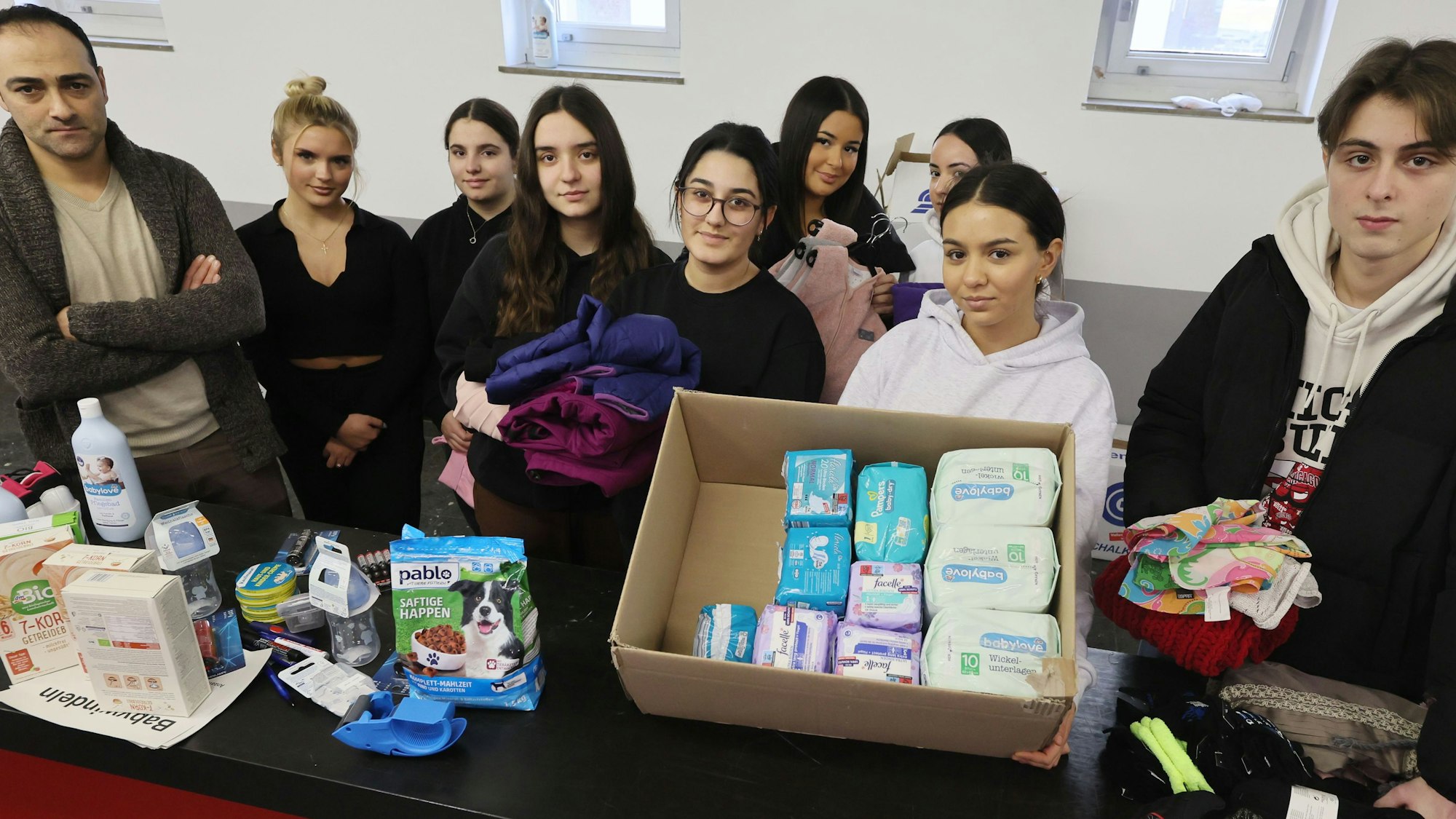 Ein Gruppe Schüler steht hinter einem langen Tisch, auf dem Hygieneartikel und andere Waren deponiert sind.