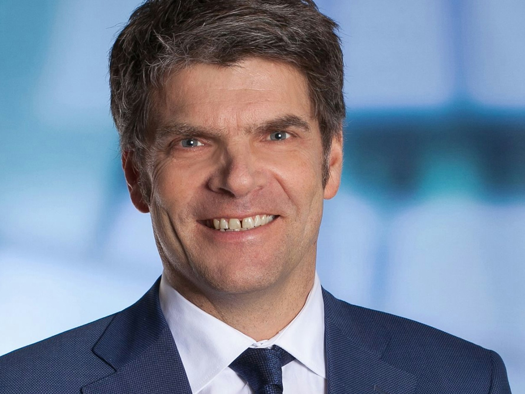 Zu sehen ist Oliver Wolff im Porträt, der Hauptgeschäftsführer des Verbands Deutscher Verkehrsunternehmen trägt Anzug und Krawatte mittelblau Ton in Ton und lächelt in die Kamera.