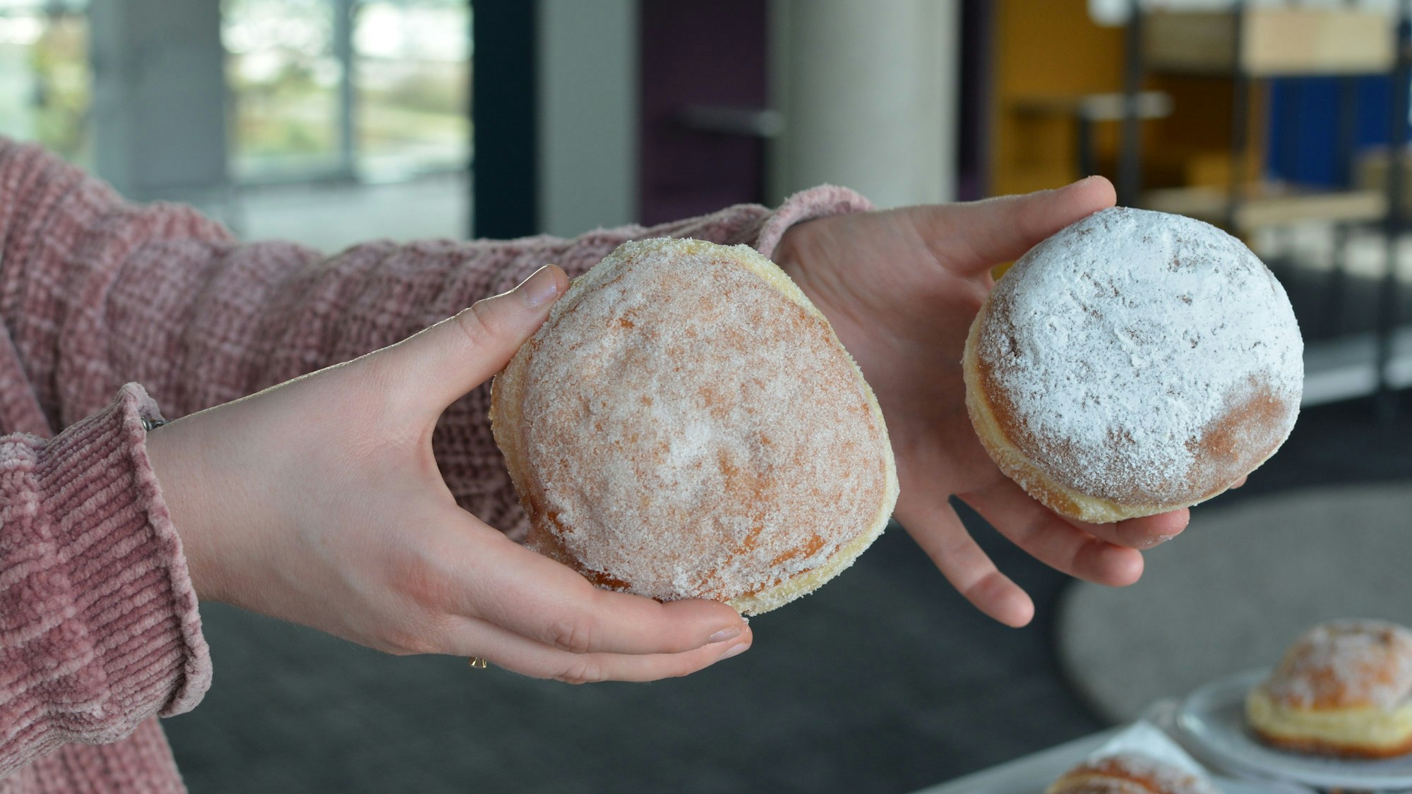 Zwei Berliner werden in der Hand gehalten zum Größenvergleich.