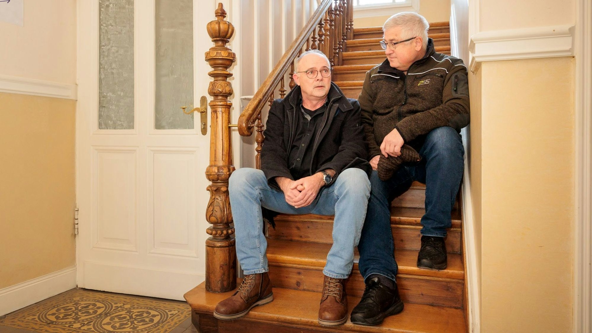 Zwei Männer sitzen auf einer alten Eichentreppe.