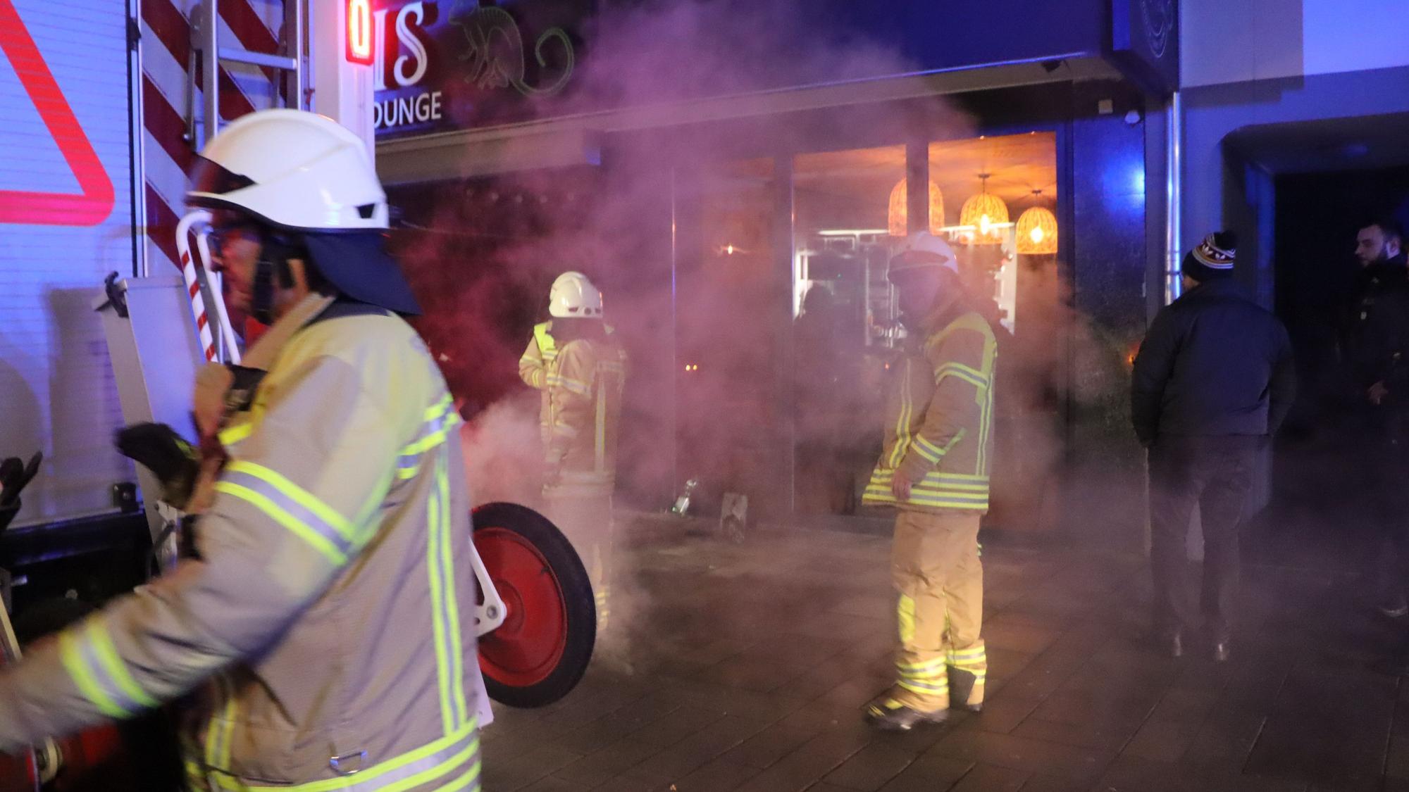 Feuerwehrleute stehen vor einem Gebäude, viel Rauch ist in der Luft.