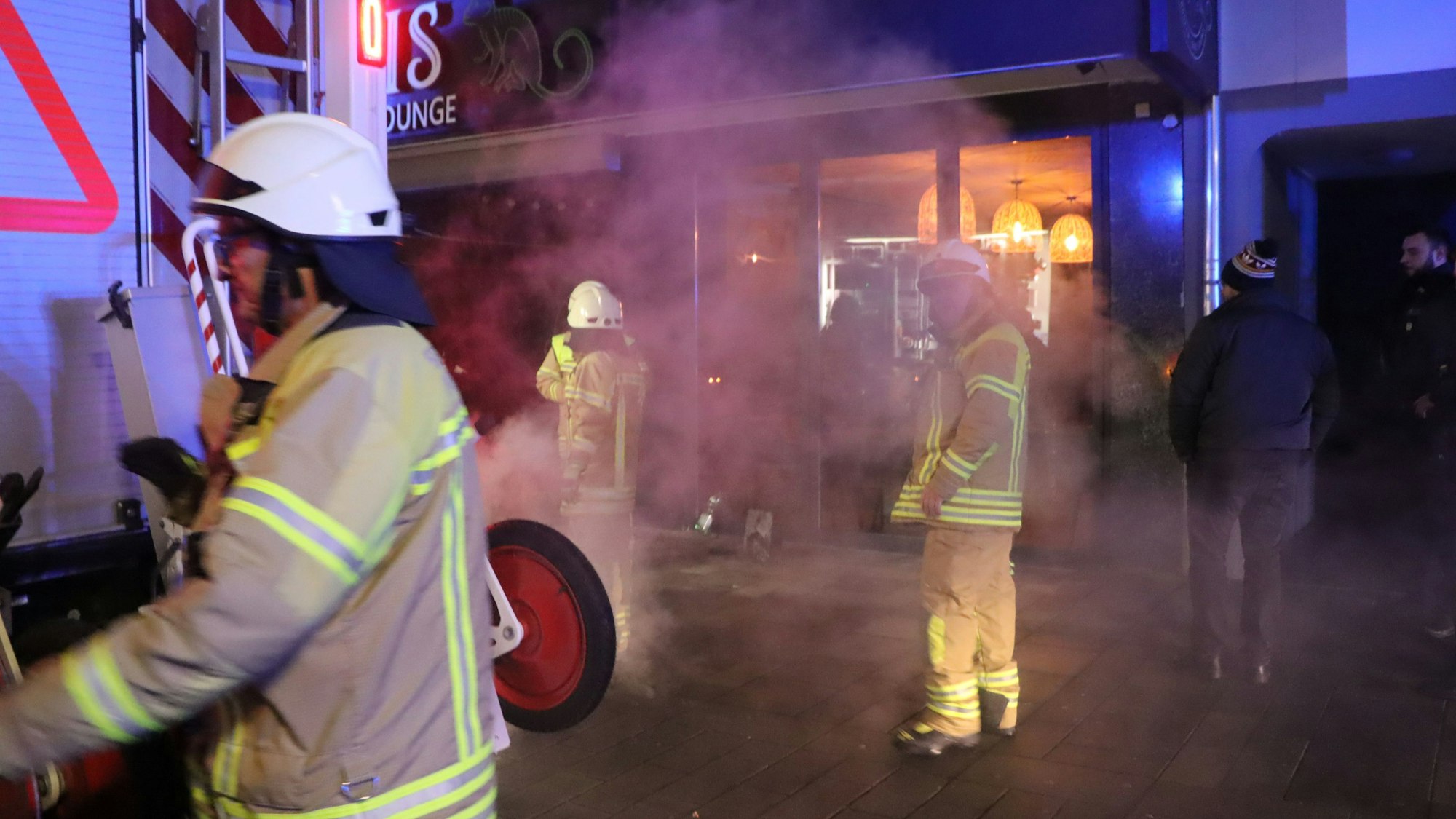 Feuerwehrleute stehen vor einem Gebäude, viel Rauch ist in der Luft.