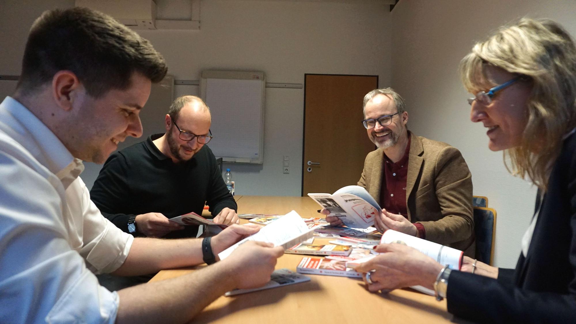 Die Leiter und Leiterinnen des DRK sitzen an einem Tisch und blättern durch Kataloge und Broschüren.