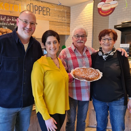 Vor einer Brottheke steht Familie Küpper. Ein Mann hält einen Kuchen in der Hand.