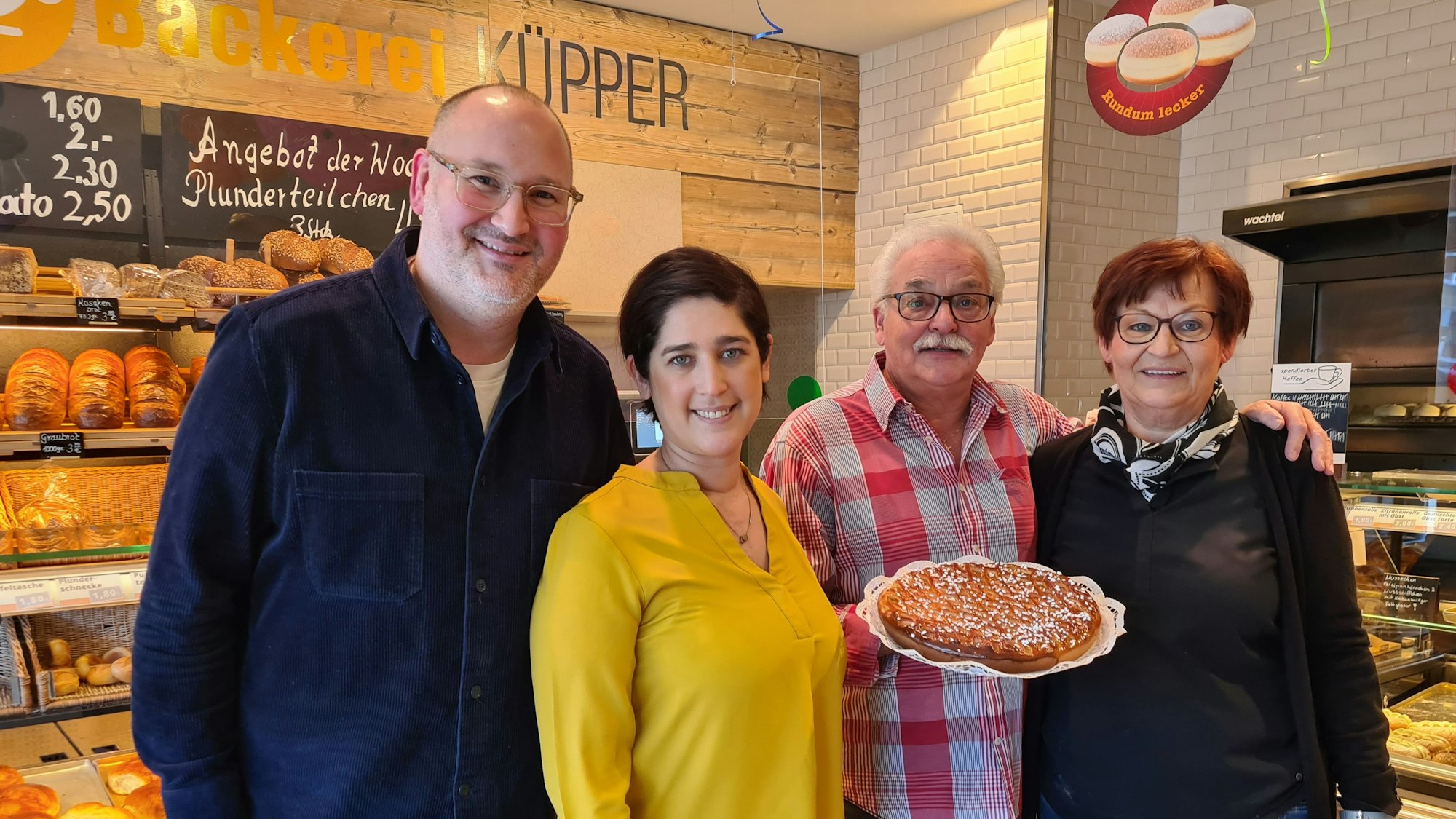 Vor einer Brottheke steht Familie Küpper. Ein Mann hält einen Kuchen in der Hand.